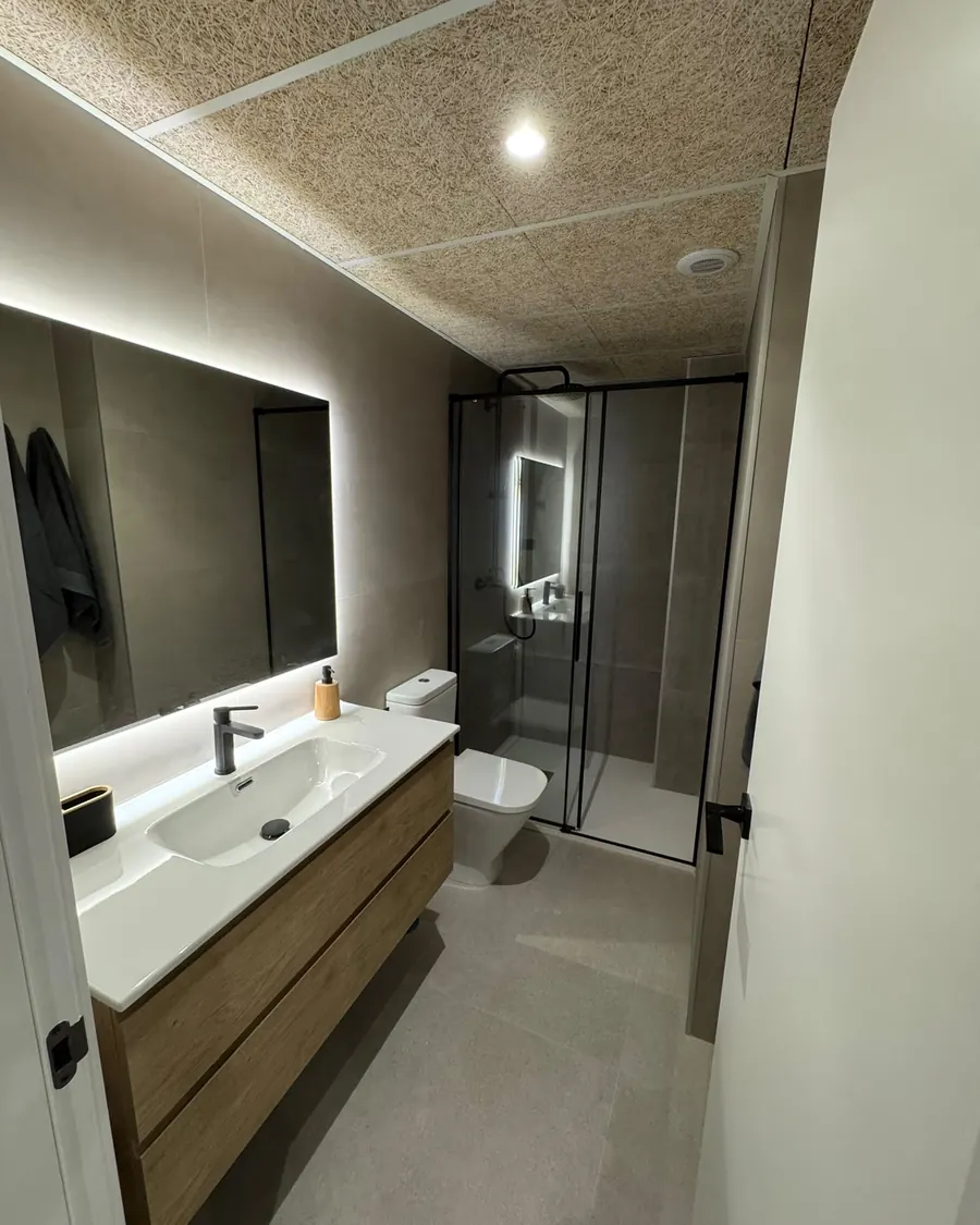 Baño reformado con mueble de madera, espejo con luz LED y ducha con mampara
