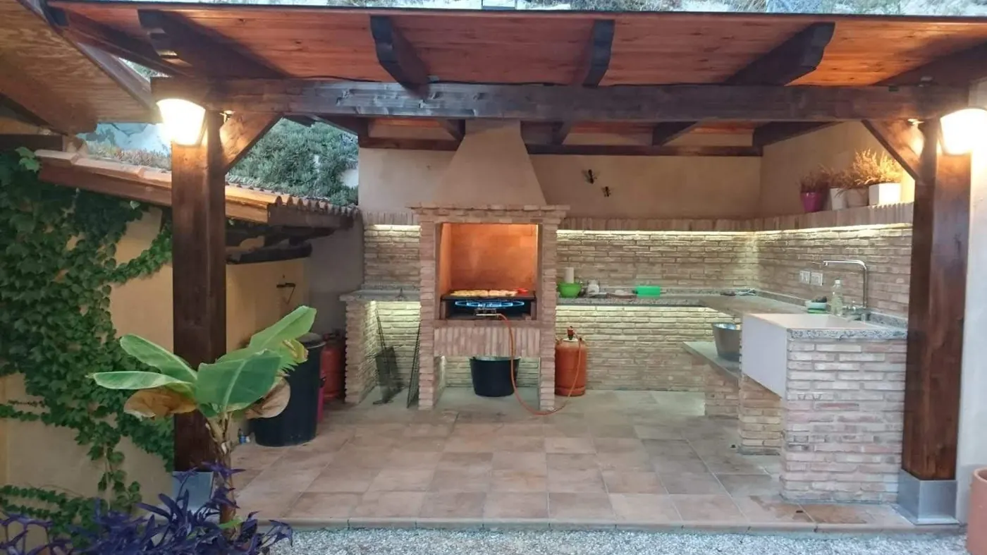 Cocina de verano terminada, con barbacoa de ladrillo, fregadero y pérgola de madera