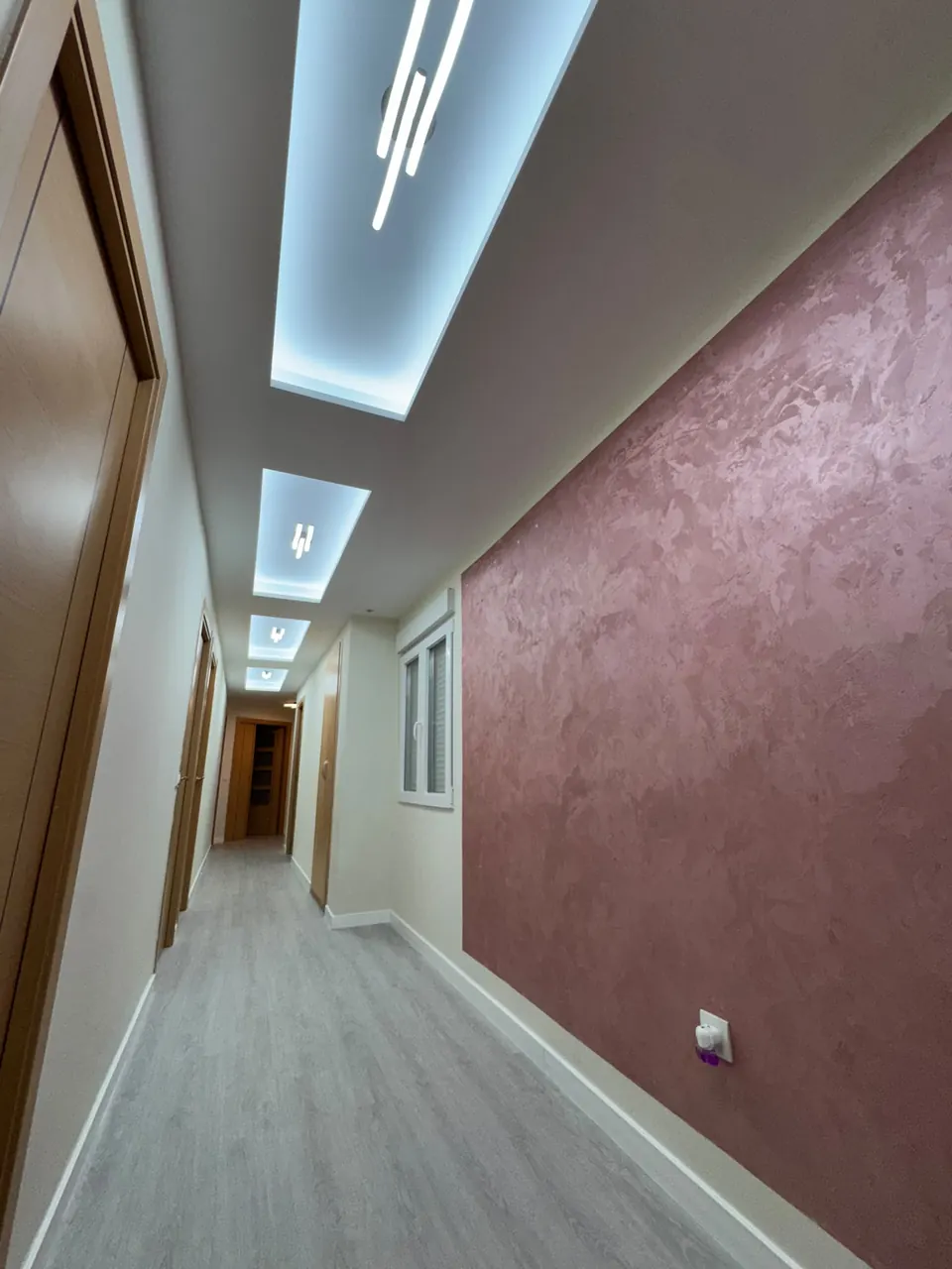 Pasillo después de la reforma: techo nuevo con iluminación LED, pared de micrometal rosa y suelo nuevo